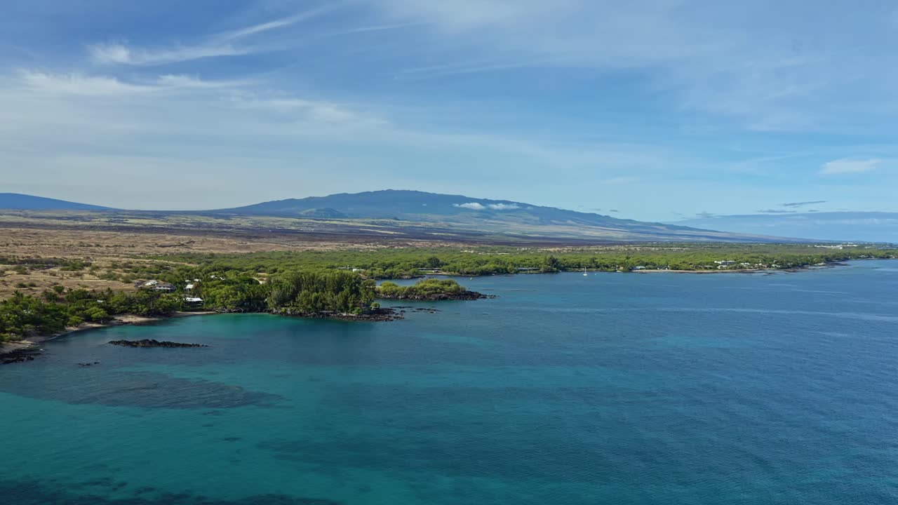 Le calme acque turchesi si estendono lungo la costa vulcanica delle Hawaii, dove il Pacifico riflette la serena bellezza dell’isola sotto la lontana silhouette di antiche montagne vulcaniche.