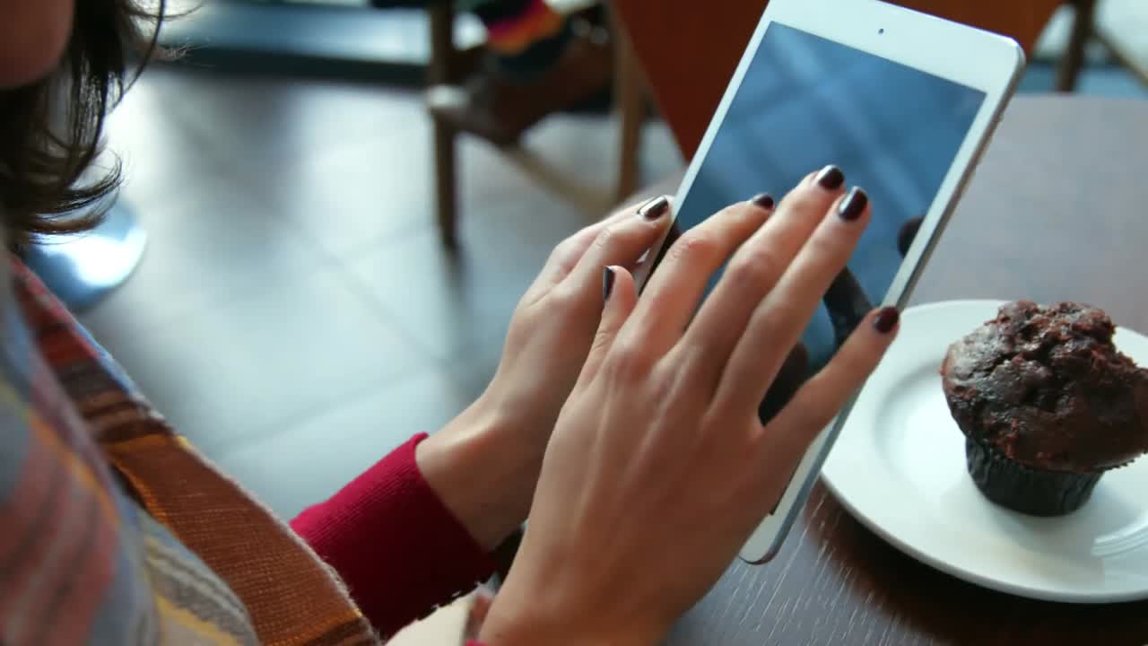 bonita morena tomando un café en una cafetería usando una tableta