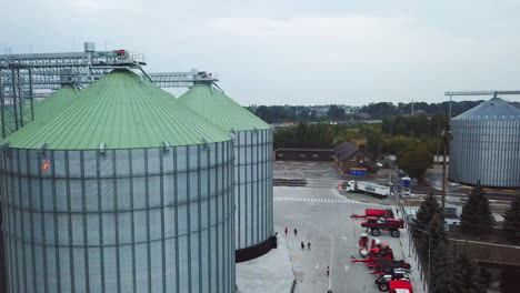 metal tanks of elevator with diverse agricultural machinery nearby. people walking along the huge silver cisterns. view from above.