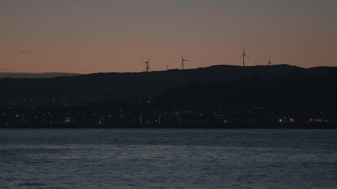 Wind Turbines Silhouetted Against Twilight Sky Overlooking a Coastal City