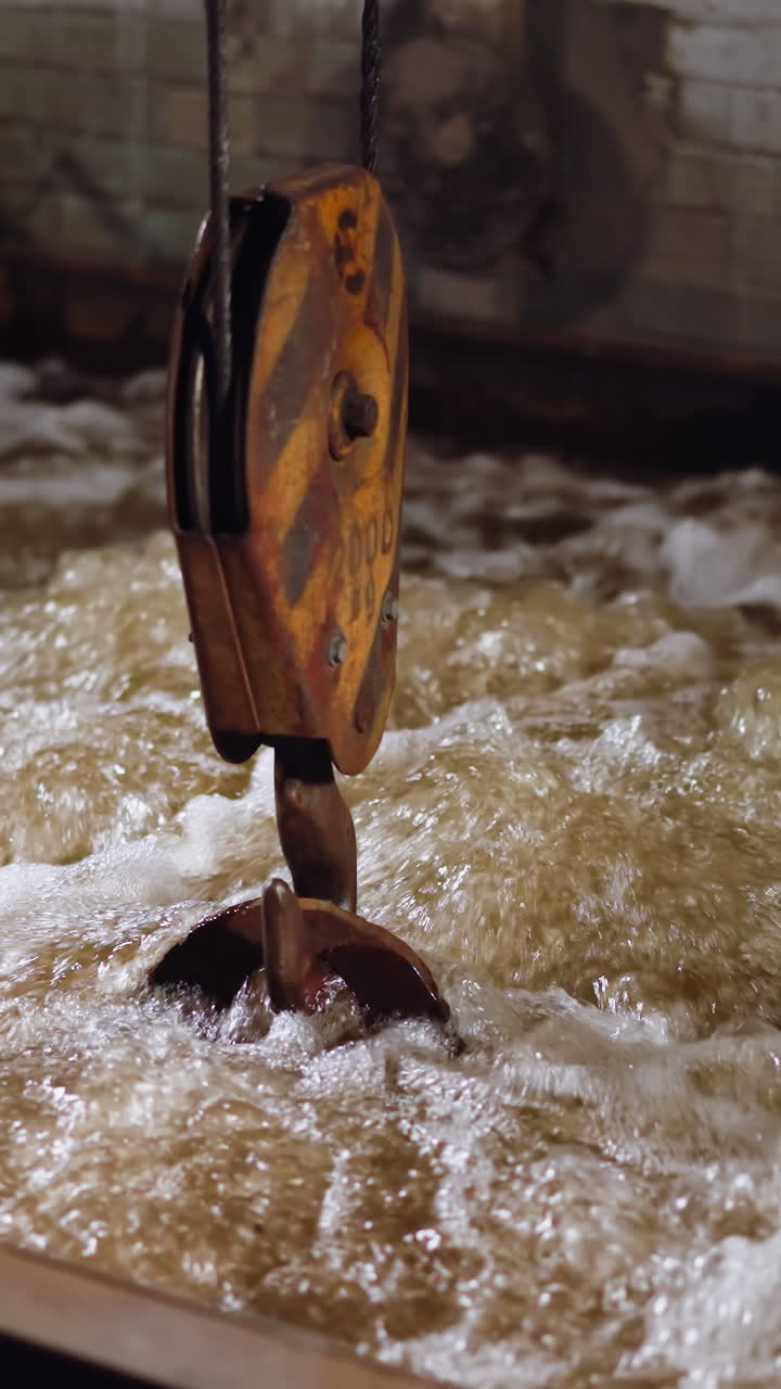 Frothy turbulent water in industrial quenching tank with crane hook, steamy atmosphere