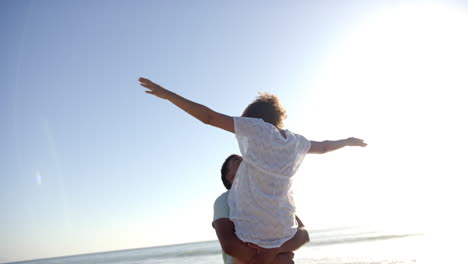 Biracial-couple-embraces-on-a-sunny-beach,-with-clear-blue-skies-overhead,-with-copy-space