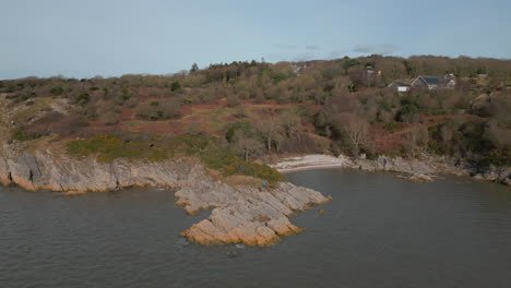 Rocky-coastline-and-small-gravel-beach-with-murky-sea-water-revealing-winter-hillside-at-Jenny-Brown's-Point-Silverdale-UK