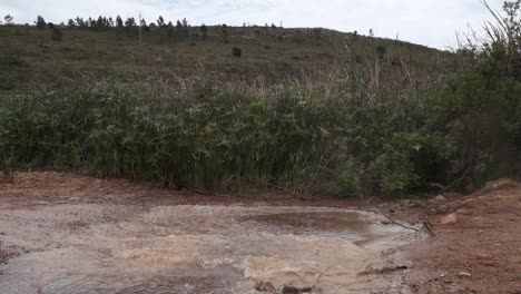 cyclists ride through a muddy puddle splashing water on a gravel road