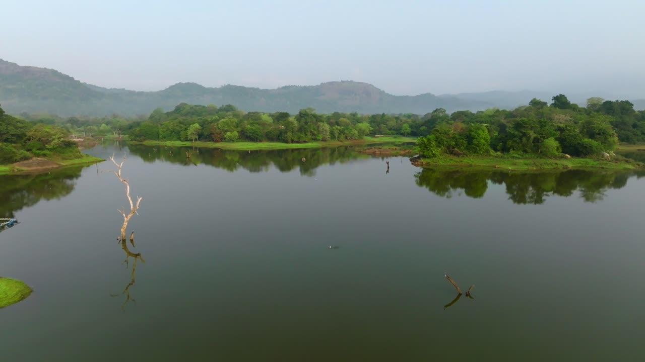 Sri Lanka elevated view of a forested peninsula curving into a still lake, layered hills in mild haze behind