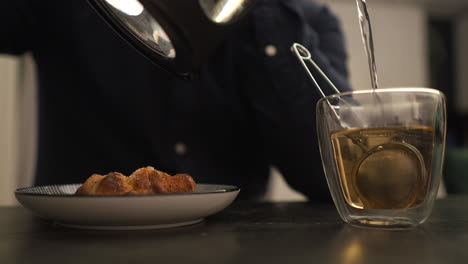 pouring hot water into a cup of tea with infuser during an evening lunch break - medium shot