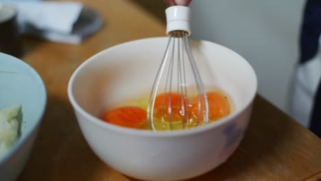 Egg-yolk-with-egg-whites-lightly-whisked-in-white-bowl,-filmed-as-as-closeup-handheld-shot