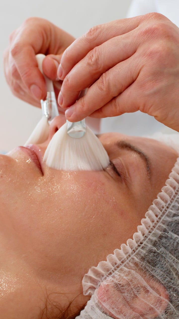 Kosmetolog påfører fuktighetsgivende peelingserum med børster på en kvinnes ansikt på en skjønnhetsklinikk.
