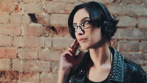 young gothic woman listening to music on headphones against the background of a brick wall in an aba