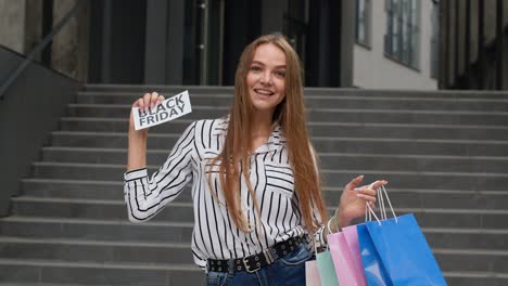 Girl-showing-Black-Friday-inscription-from-shopping-bags,-looking-satisfied-with-low-prices.-Outdoor