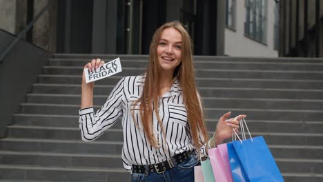 girl showing black friday inscription from shopping bags, looking satisfied with low prices. outdoor