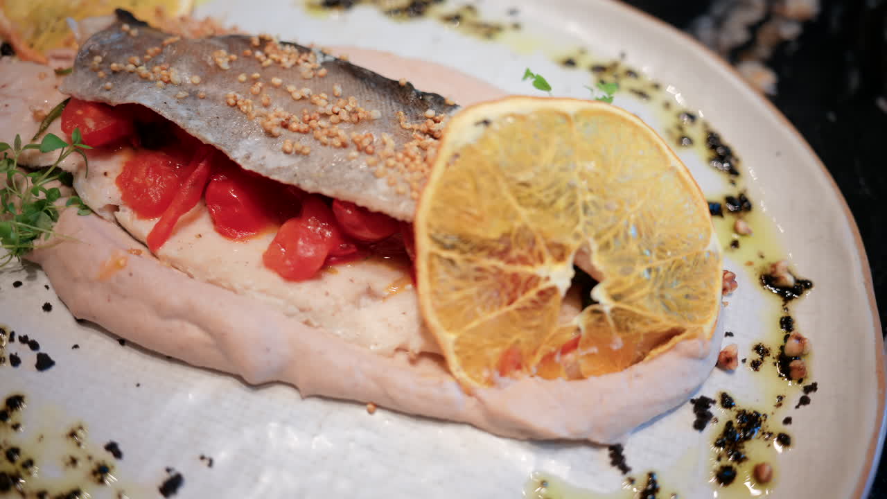 Primo piano di un filetto di pesce impiattato con cura, con salsa, fetta di limone ed erbe aromatiche