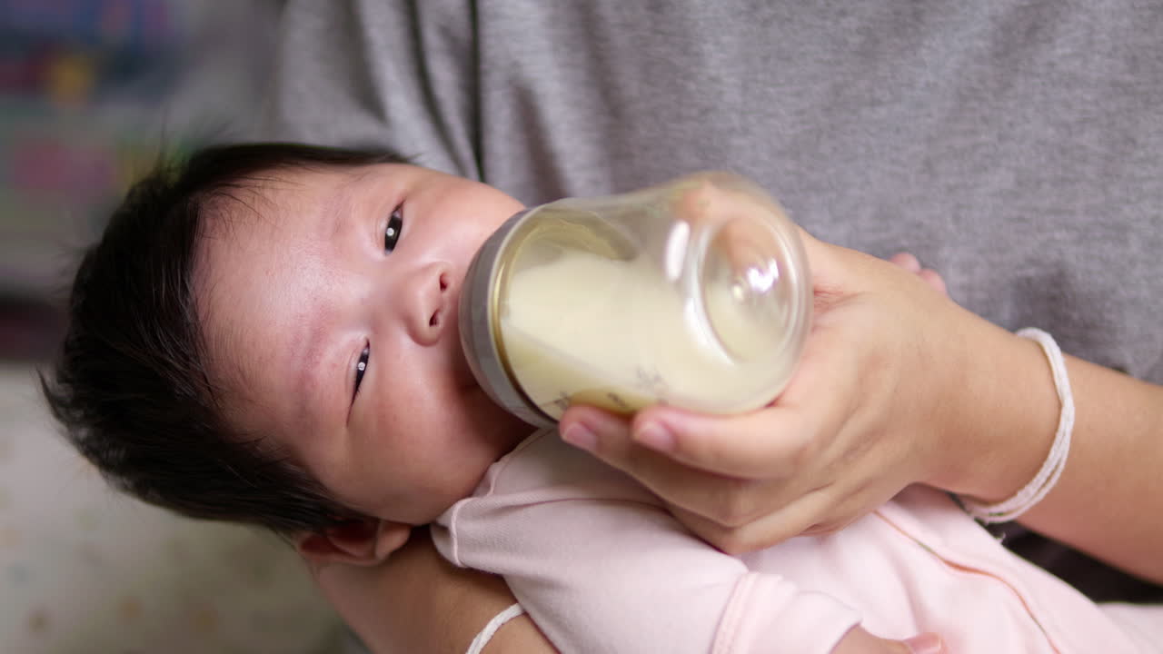 Close-Up of 2-Month-Old Baby Girl Suckling Milk from a Bottle: Slow Motion Shot of Mother Tenderly Feeding Her Baby
