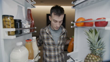 a young man takes a bottle of juice from the refrigerator. view from inside the refrigerator