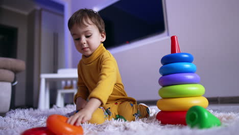 focused little boy collecting pyramid. beautiful toddler playing with toys at home. low angle view.