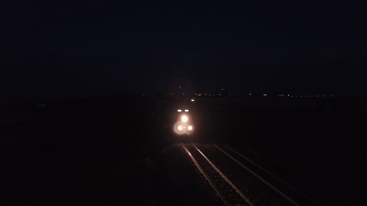 el tren de carga ilumina las vías del tren de la pradera en la noche púrpura oscura