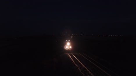 El-Tren-De-Carga-Ilumina-Las-Vías-Del-Tren-De-La-Pradera-En-La-Noche-Púrpura-Oscura