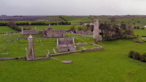 dynamic aerial shot approaches old round towers and buildings at clonmacnoise