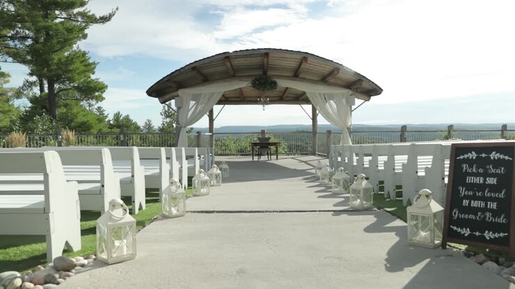 Elegant out door wedding ceremony venue with white lanterns as décor and white benches in front of a beautiful arching pergola over looking the Gatineau Hills at Le Belvédère in Wakefield, Quebec