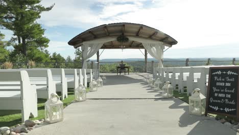 elegant out door wedding ceremony venue with white lanterns as décor and white benches in front of a beautiful arching pergola over looking the gatineau hills at le belvédère in wakefield, quebec