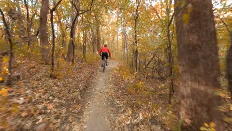 fpv drone, mountain biker biking on a dirt path in forest during autumn season