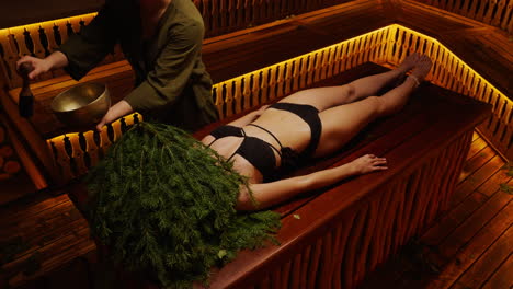 Woman receiving a traditional sauna treatment with herbal therapy and sound healing.