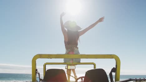 Happy-caucasian-woman-sitting-on-beach-buggy-by-the-sea-waving-hands