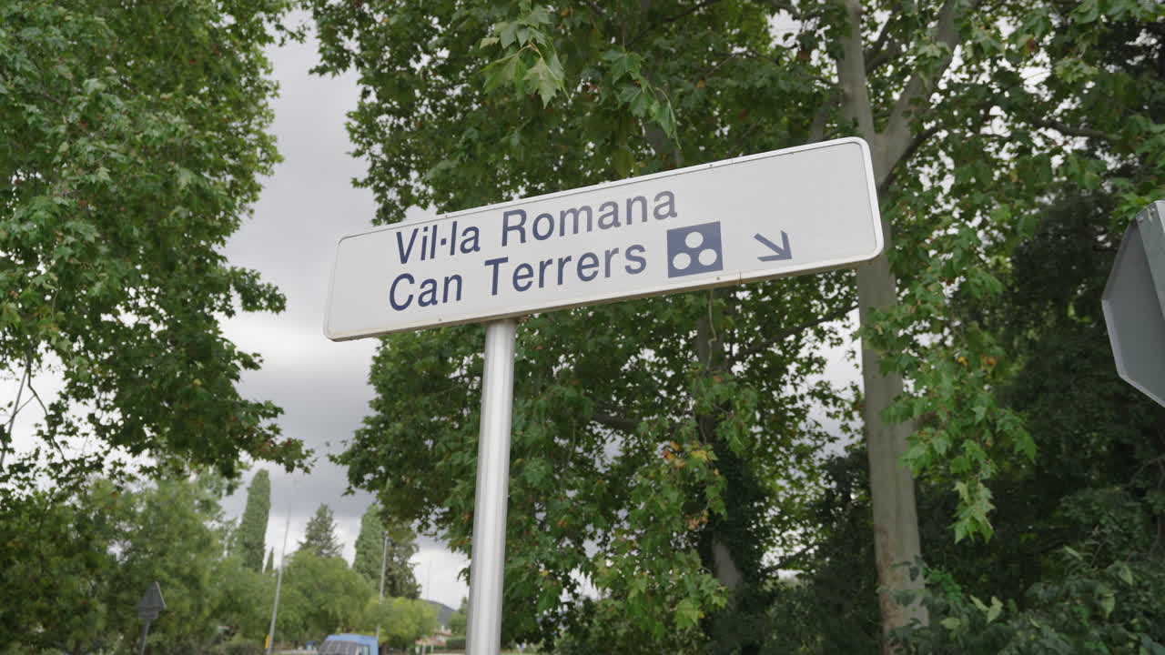 Scopri il segnale stradale che indica Villa Romana Can Terrers a Barcellona, circondata da una vegetazione lussureggiante