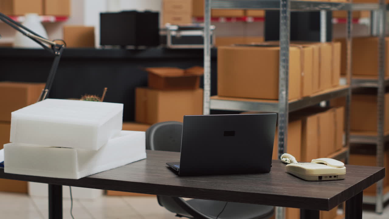 Mesa de escritório em armazém com laptop, telefone e caixas