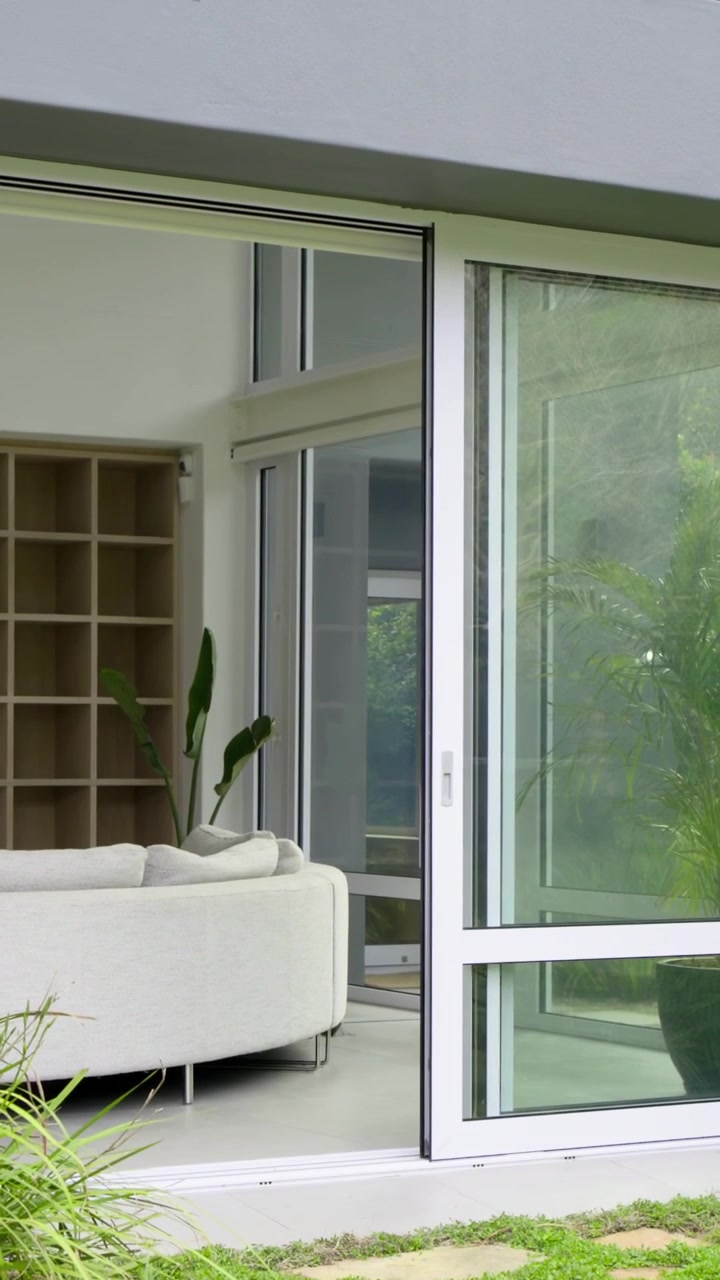 Video vertical: Cámara inclinándose mostrando una puerta corredera con ventana a dos aguas gris, un sofá y plantas en casa.