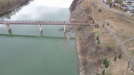 3-3-Vuelo-Aéreo-Sobre-El-Parque-Fluvial-Por-Un-Puente-Peatonal-Multimaterial-De-Madera-De-Hormigón-Y-Acero-En-Una-Tarde-De-Otoño-Donde-Suele-Estar-Ocupado-Pero-Debido-A-Las-Restricciones-De-Cierre-De-Covid-19-Es-Tranquilo