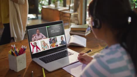 schoolgirl using laptop for online lesson at home, with diverse teacher and class on screen