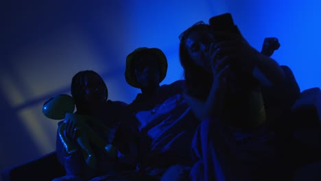 studio shot of group of gen z friends sitting on sofa posing for selfie on mobile phone at night with flashing light 2