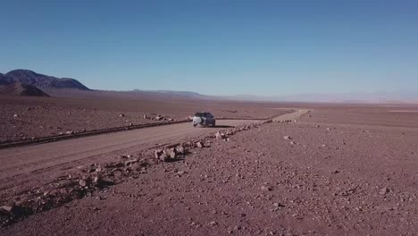 Car-driving-on-a-dusty-road-in-the-Atacama-Desert-with-an-arid-landscape-in-Northern-Chile
