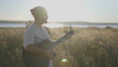 man playing guitar in a field at sunset