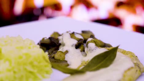 chicken-cutlet-with-cream-and-mushrooms,-fresh-cream,-cheese,-rice-in-a-square-plate-with-a-wood-fire-in-the-background