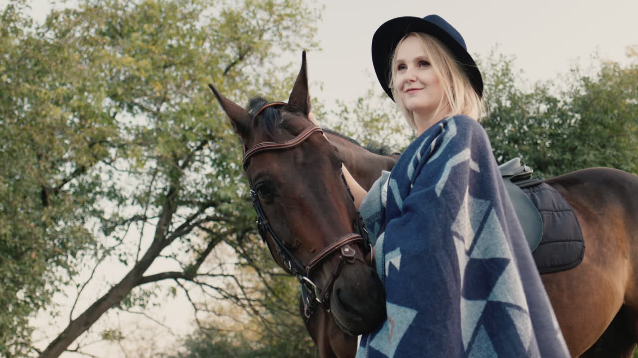 retrato de una mujer elegante con sombrero y poncho cerca de un caballo