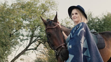 retrato de una mujer elegante con sombrero y poncho cerca de un caballo