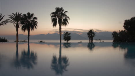 timelapse of evening on resort pool palms and scene with sea and mountains