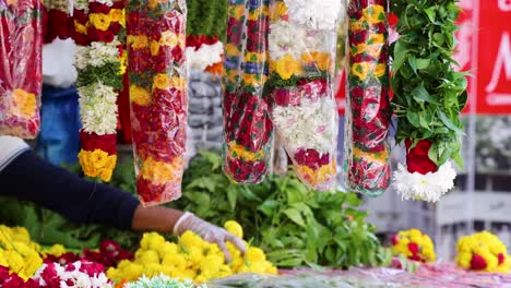 a vendor arranges vibrant marigold and mixed flower garlands at an outdoor market stall in singapore, with bright natural lighting and a steady camera angle