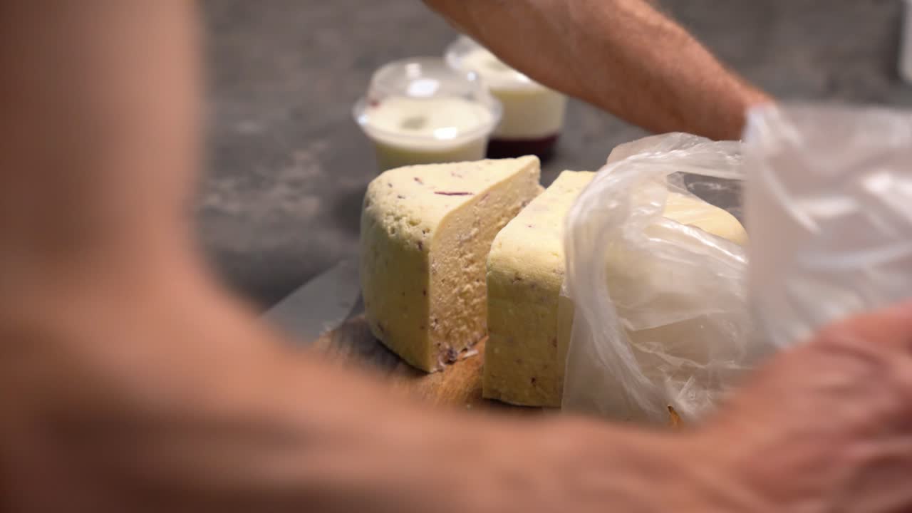 Hands slicing artisan cheese block on wooden board preparing dairy products