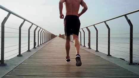 young attractive athlete running away half naked on a bridge in the morning from a perspective point of view in slow motion