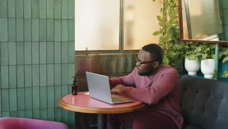 hombre afroamericano usando una computadora portátil y tomando notas en un café