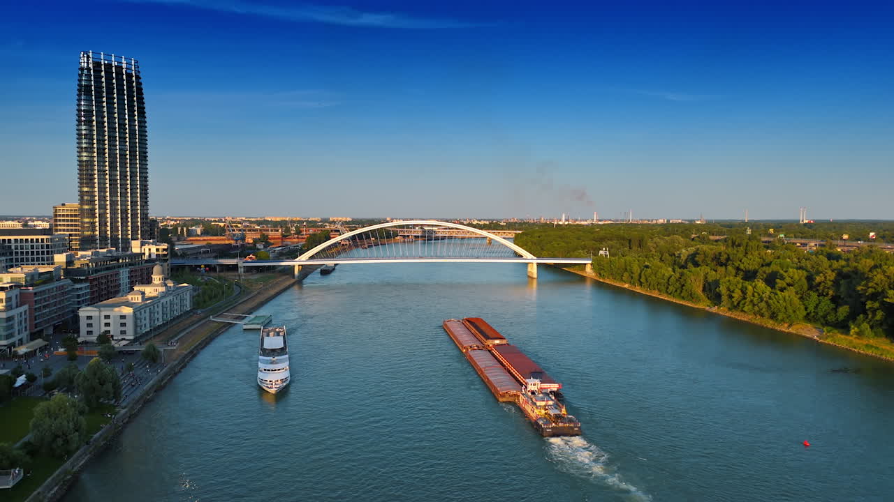 Barge pushing the loads by the Danube towards the Appolo Bridge. Riverboat travel along the shore. Aerial view. Bratislava, Slovakia