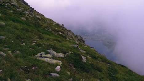 Großer-Kameraschwenk-Vom-Grünen-Hügel-Aus,-Der-Durch-Die-Wolken-Blickt-Und-Einen-See-Unten-Freigibt