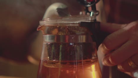 Close-up of a hand picking dried tea leaves to brew with a glass tea press. Ideal for themes of traditional tea rituals, craftsmanship, and slow-living moments.