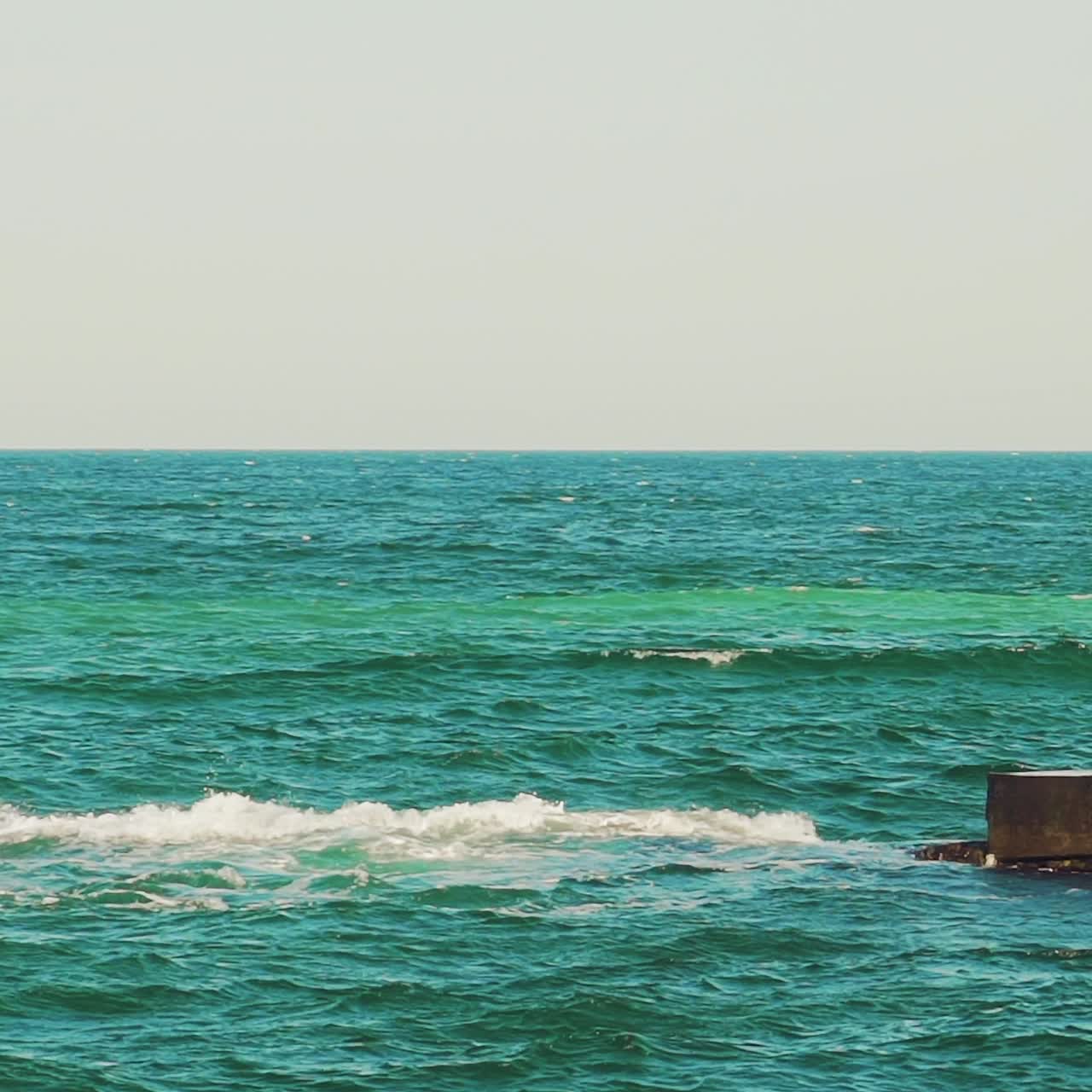 a white sailboat is floating in the sea near the coast on the background of an old pier in the summer. Seascape. Slow motion