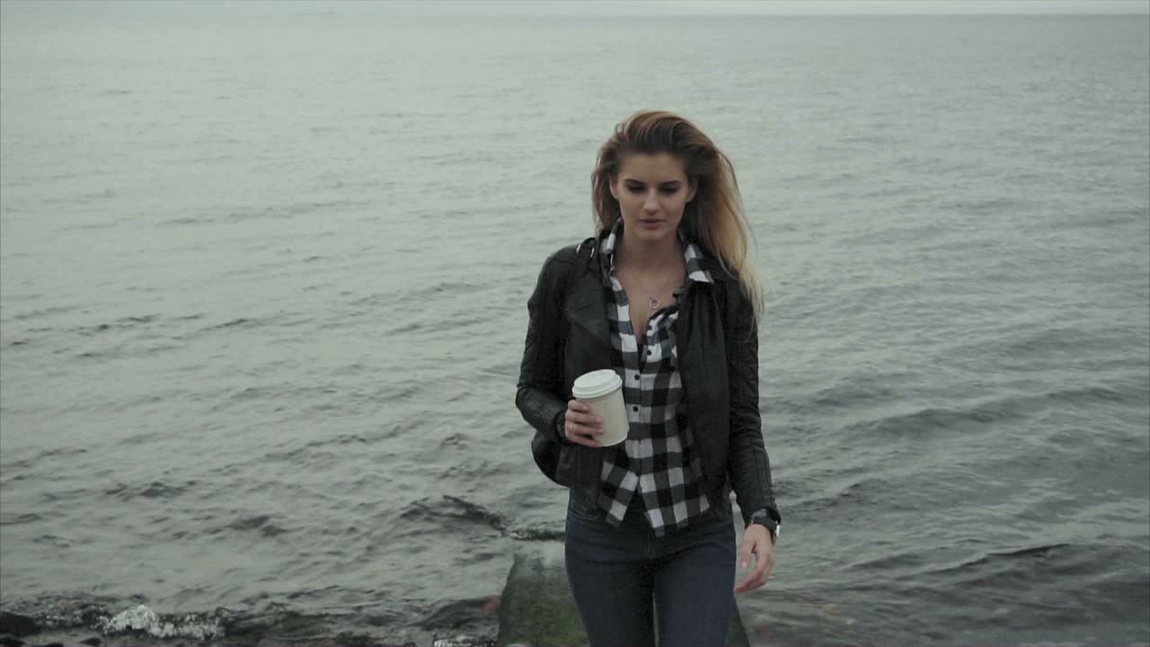 mujer caminando por la playa con café