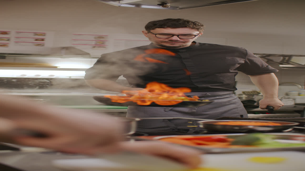 Chef professionista che cucina con una padella in fiamme nella cucina di un ristorante