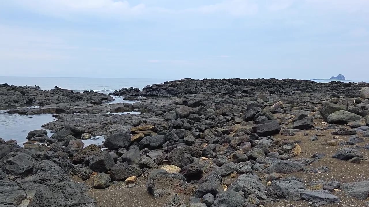 韓国、済州島の龍頭海岸（ヨンモリ海岸）近くのサゲ海岸の海岸線を覆う黒い火山性玄武岩。地平線には海食柱が見える。